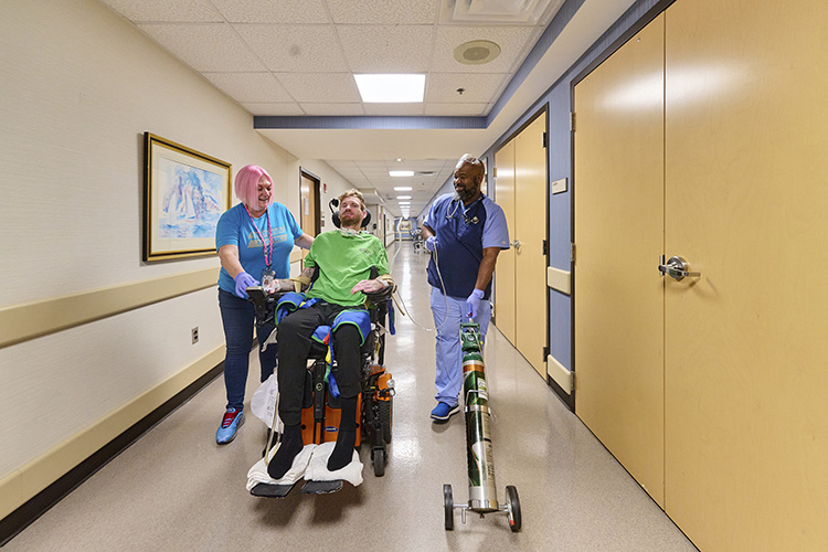 Brandon, a patient reliant on a ventilator, navigates the corridors of Shepherd Center with the dedicated support of his respiratory therapists, Kelley and Mychal. 